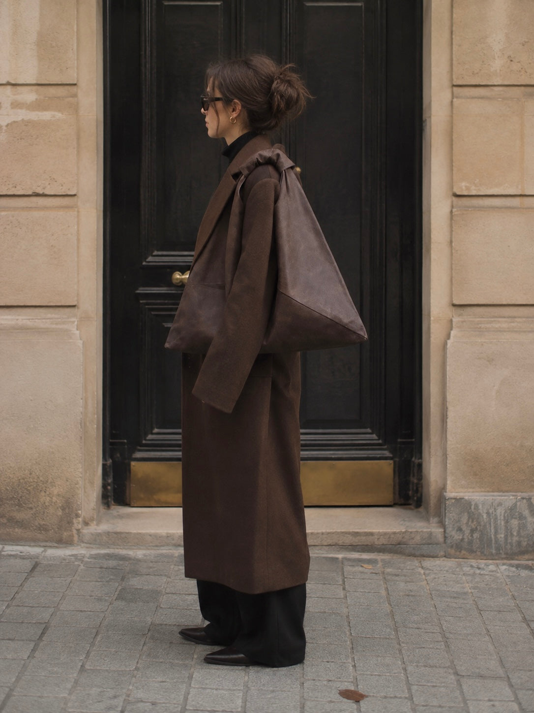 Model standing in front of a wooden door with a Esra Kayira dark brown waxed canvas origami bag.